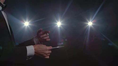 Moving Hands of an Orchestra Conductor Directing Musicians with Movement of Baton on Black