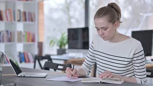 Jeune femme lisant un livre et faisant de la paperasse à la bibliothèque