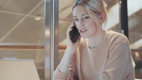Female Office Worker Talking on Phone and Using Laptop