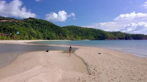 Mulher em traje de banho preto caminhando e depois correndo sozinha em um banco de areia na Tailândia