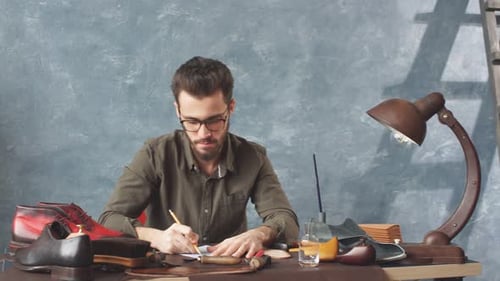 Man Designs Leather Shoes at Workshop Desk