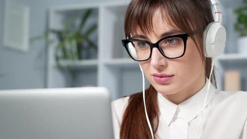 Young woman in headphones works looking at the laptop screen.
