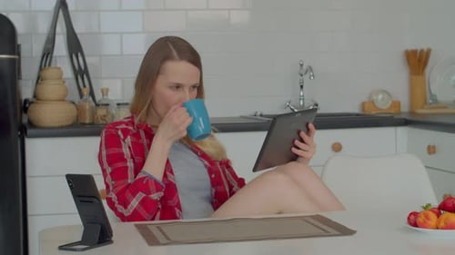 Woman Using Tablet and Drinking Coffee in Kitchen