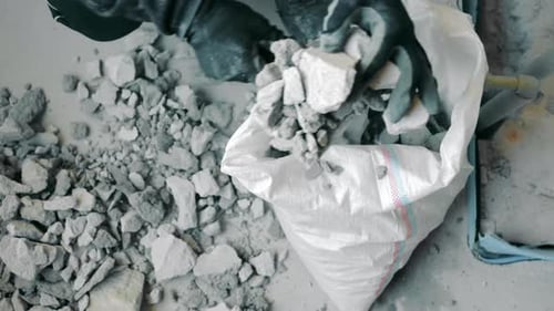 A Man Collects the Remains of Construction Waste at a Construction Site in a Bag