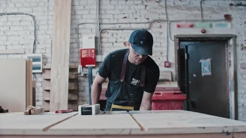 Man in Protective Glasses in Carpentry Workshop Cutting a Small Wooden Detail in Pieces Using a