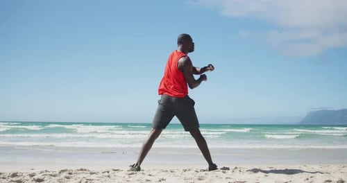 African american man stretching on the beach, exercising outdoors by the sea