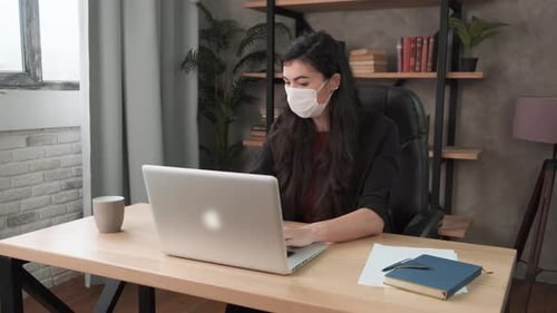 Young Business Woman Coughs Into Protective Face Mask Working in the Office. Brunette Girl with