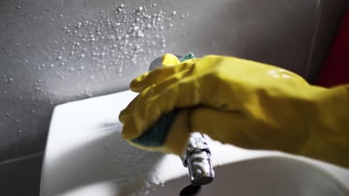 Cleaning Faucet with Yellow Glove and Sponge