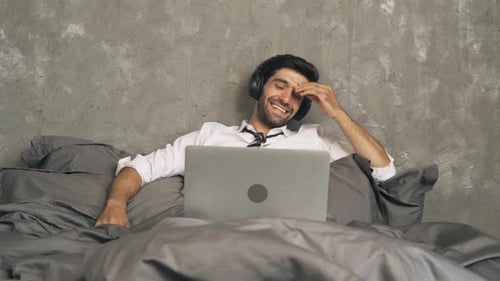 Man Laughing in Bed with Laptop and Headphones