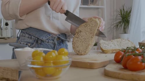 Woman Cutting Bread in Kitchen with Tomatoes
