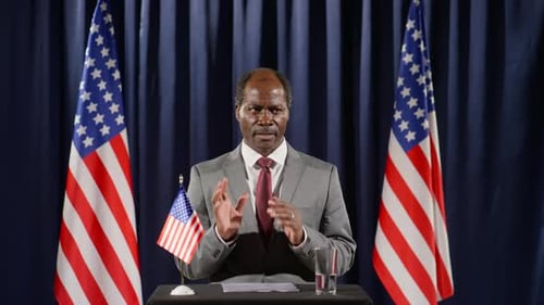 Speaker Addresses Audience Behind Podium with Flags