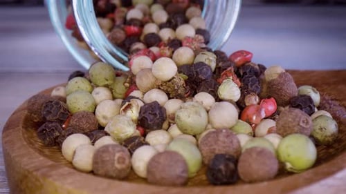 Multi-Colored Peppercorns Spilling into Wooden Bowl