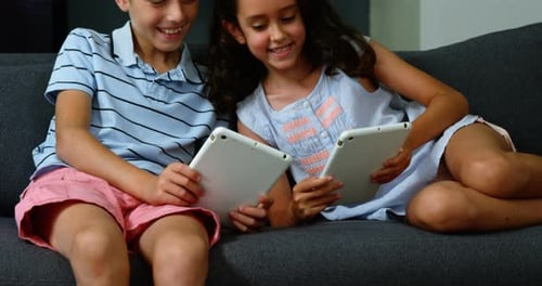 Two Children Play on Tablets on a Couch