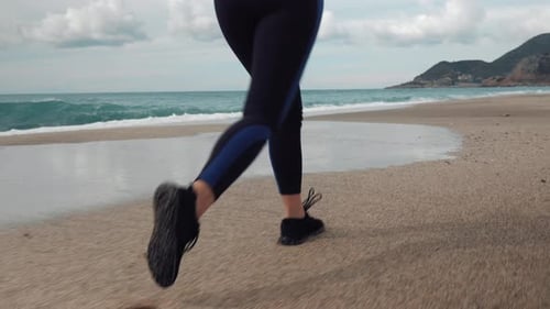 Female legs are running on sandy beach