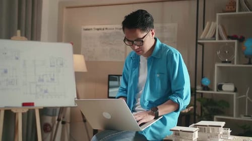 Asian Man Engineer Sitting On The Table And Using A Laptop To Work At The Architectural Office