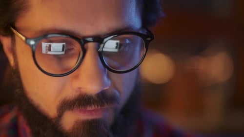 Portrait Of a Man Is Working On Laptop Computer With Glasses At Night. Close Up. Businessman Looking