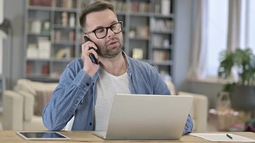 Man Talks on Phone While Using Laptop at Desk