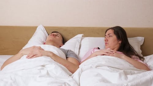 Une femme se couche près d'un homme ronflant et couvre l'oreille avec un