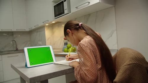 Girl Doing Homework with Tablet in Kitchen