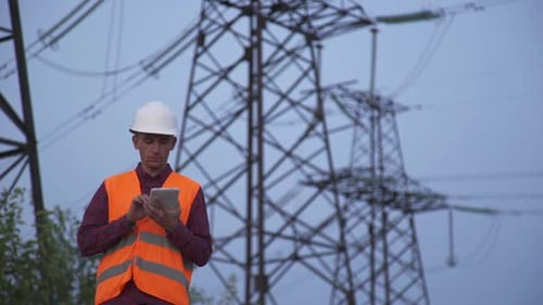 Engineer Inspecting Power Lines with a Tablet