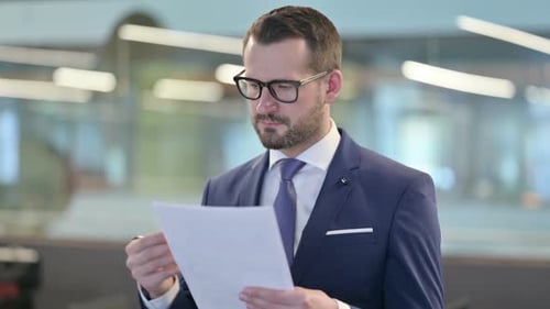 Attentive Businessman Reviewing Documents in Modern Office