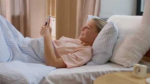 Young Woman Relaxing in Bed with Smartphone