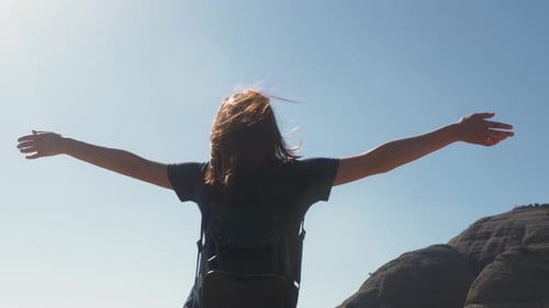 Young Woman Tourist with Backpack Standing on Cliff's Edge Top Mountain with Raised Hands and