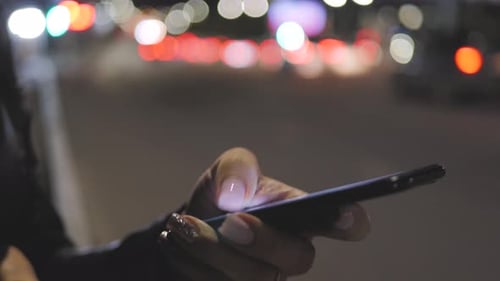 Close Up Woman Using Smartphone in the City at Night Time. Girl Looks at the Smartphone Screen