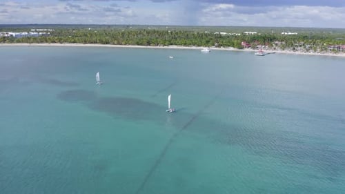 Aerial orbiting shot of sailing Catamaran on clear Caribbean Sea at Playa Nueva Romana in summer