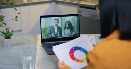 Femme assise devant un ordinateur pendant un briefing vidéo avec ses partenaires commerciaux