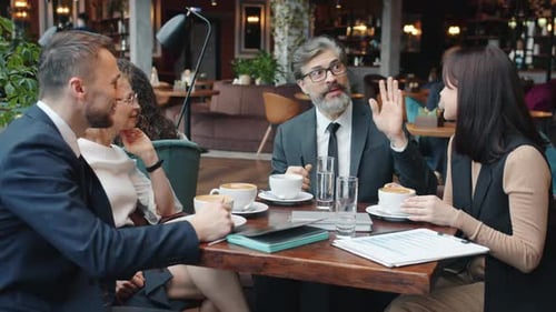 Joyful Businesspeople Women and Men Talking and Laughing at Table in Cafe