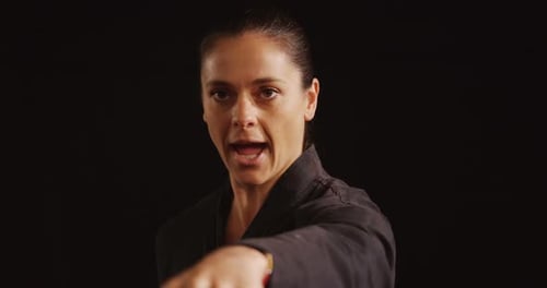 Focused Woman Karate Punches on Black Background
