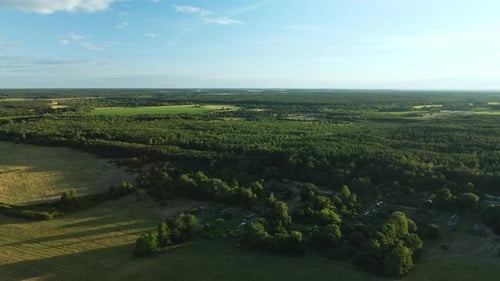 Flight Over The Forest. Houses Are Visible Among The Trees. In The Light Of The Setting Sun