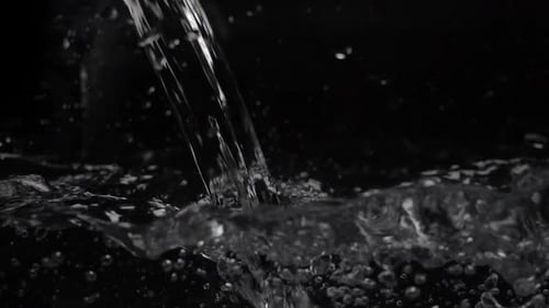 Macro Footage of Water Pouring in a Transparent Container. Black Background. Close-up Macro Shot