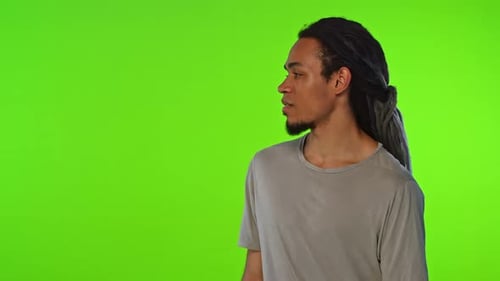 Young African American Man Looks Around and Winks Stands on Green Background