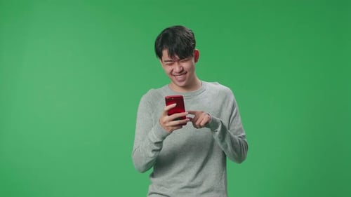 An Asian Man Enjoy Using Mobile Phone While Standing On Green Screen In The Studio