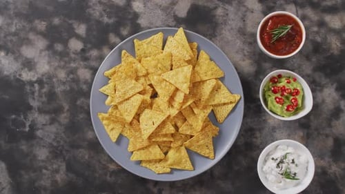 Primer plano de nachos en un plato y salsas sobre una superficie negra