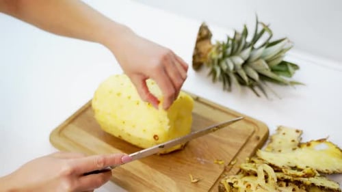 Hands Cutting Pineapple with Knife on Cutting Board