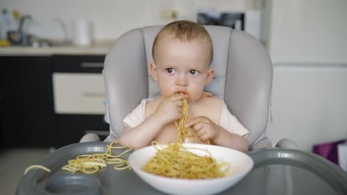 Lindo niño pequeño come espaguetis con gusto y se ensucia con salsa roja