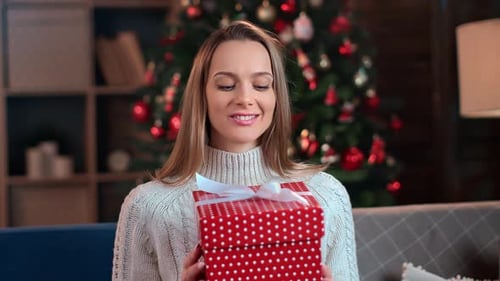 Woman Holding Christmas Present in Front of Tree