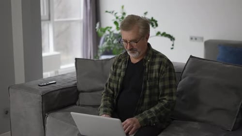 Man Uses Laptop Computer on Couch at Home