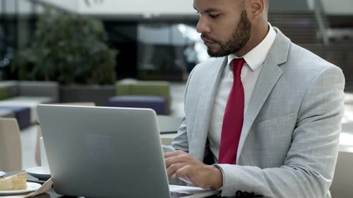Serious Young Man Typing on Laptop at Cafe