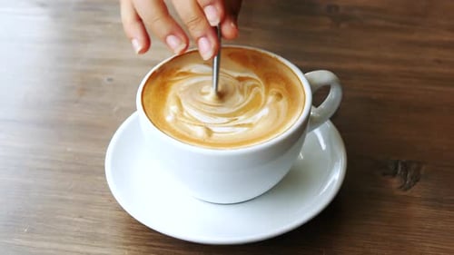 Stirring a Coffee with Cream in White Mug