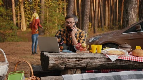 Man Works at Picnic While Family Plays