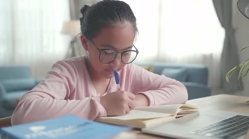 Asiatisches Mädchen mit Laptop macht Hausaufgaben im Wohnzimmer, Kind lernt online zu Hause
