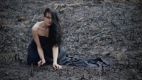 Woman Kneeling in Burnt Landscape Wrapped in Black Fabric