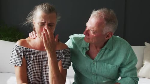 Portrait of caucasian senior woman crying while her husband supporting her at home