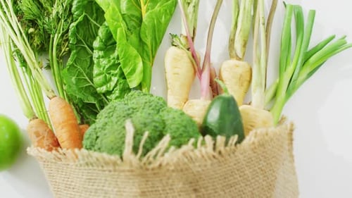 Vídeo de verduras frescas y manzana en bolsa rústica sobre fondo blanco