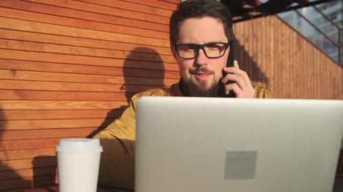 Man Talks on Phone While Working on Laptop