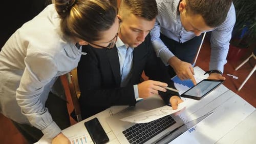 Primer plano del grupo de empleados que comparan el gráfico de resultados de ventas en papel con el gráfico en la pantalla de una tableta